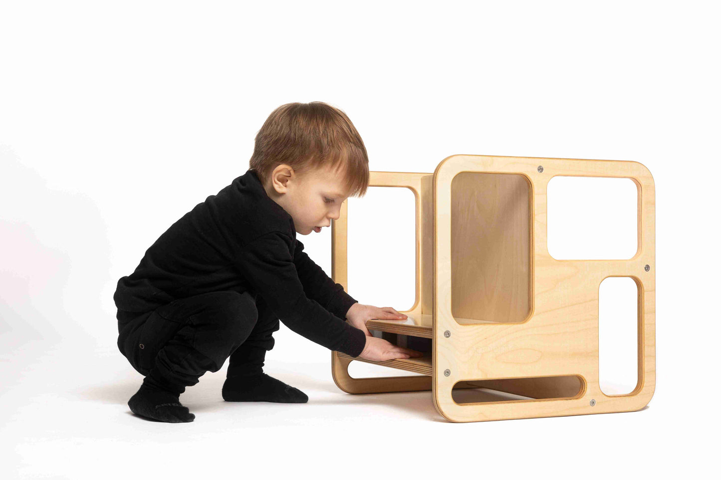 Przykucnięty chłopiec ustawia krzesełko wielofunkcyjne WoodU na odpowiednią wysokość