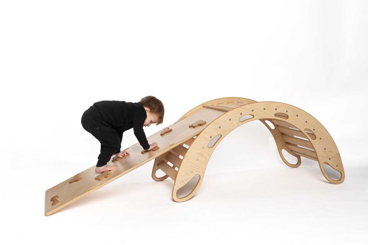 Małe dziecko wspinające się po drewnianej ściance wspinaczkowej do bujaka WoodU, białe tło