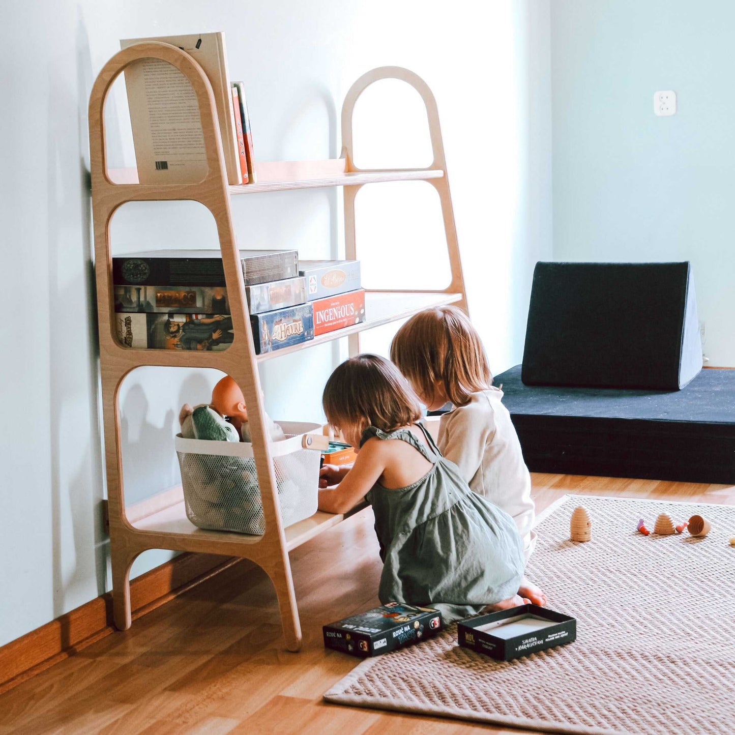 Dwoje dzieci bawiących się przy niskim regale WoodU z trzema półkami w jasnym pokoju