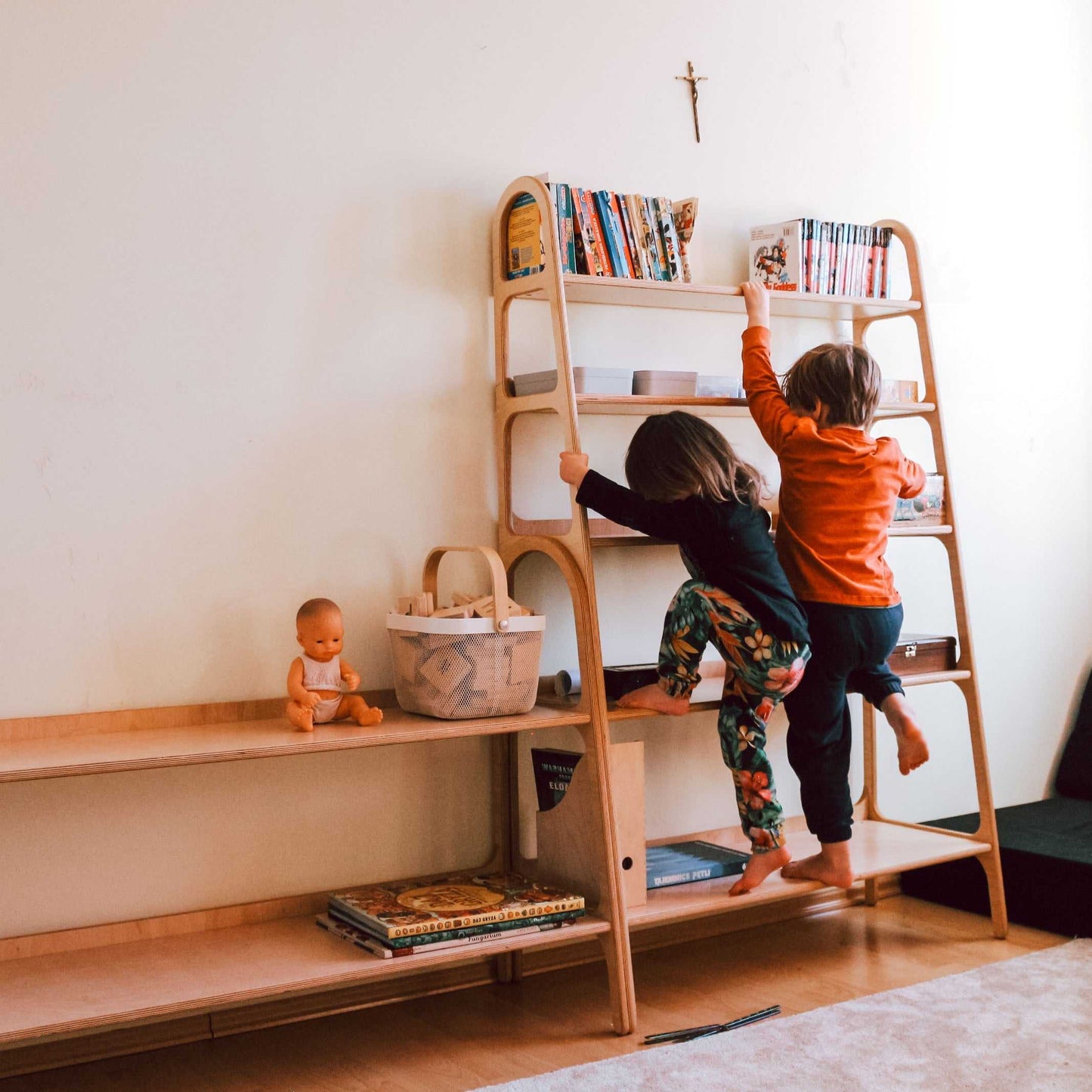 Dzieci sięgające po książki na wysokim, drewnianym regale WoodU w domowym pokoju