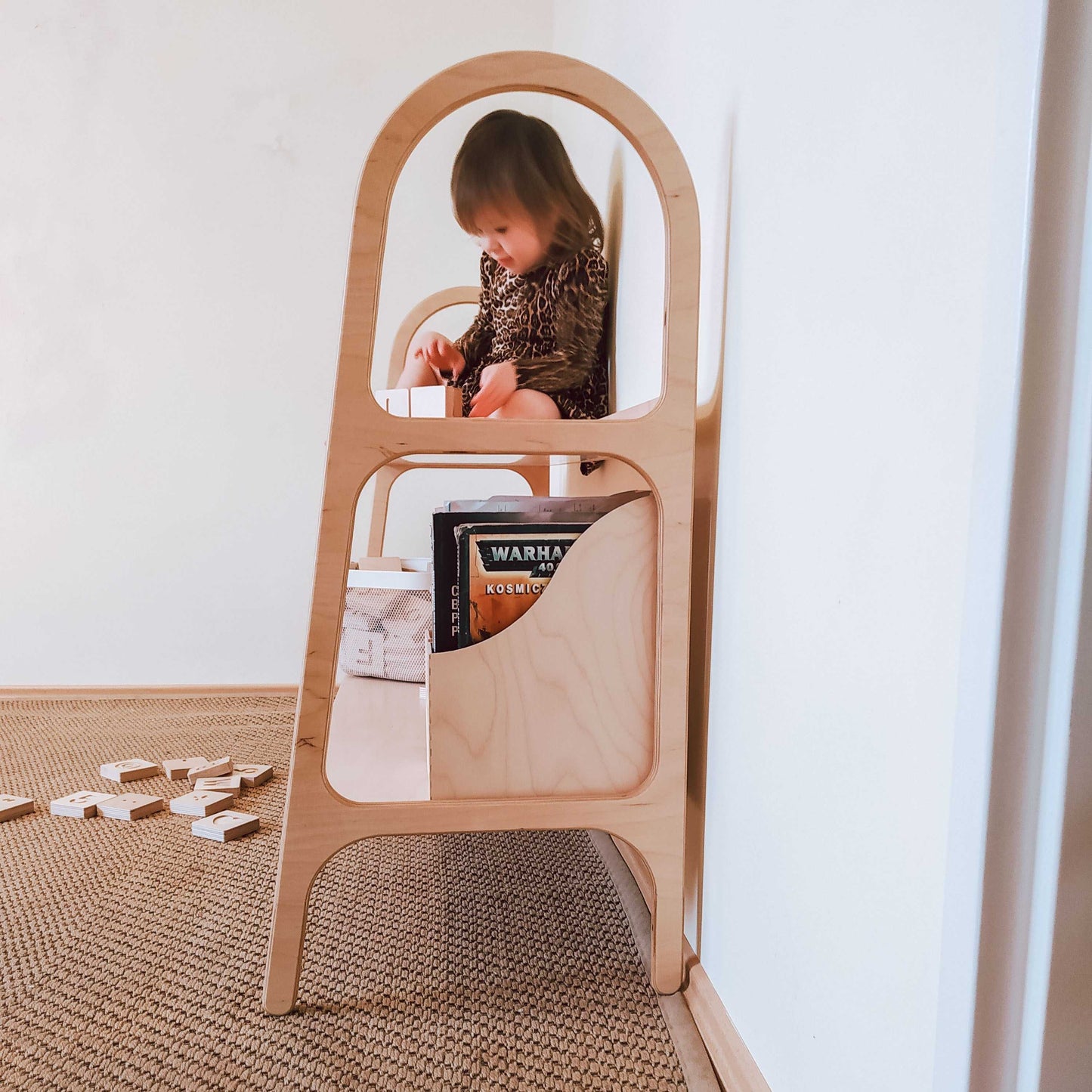 Mała dziewczynka siedząca na górnej półce regału WoodU z dwiema półkami, widok z boku